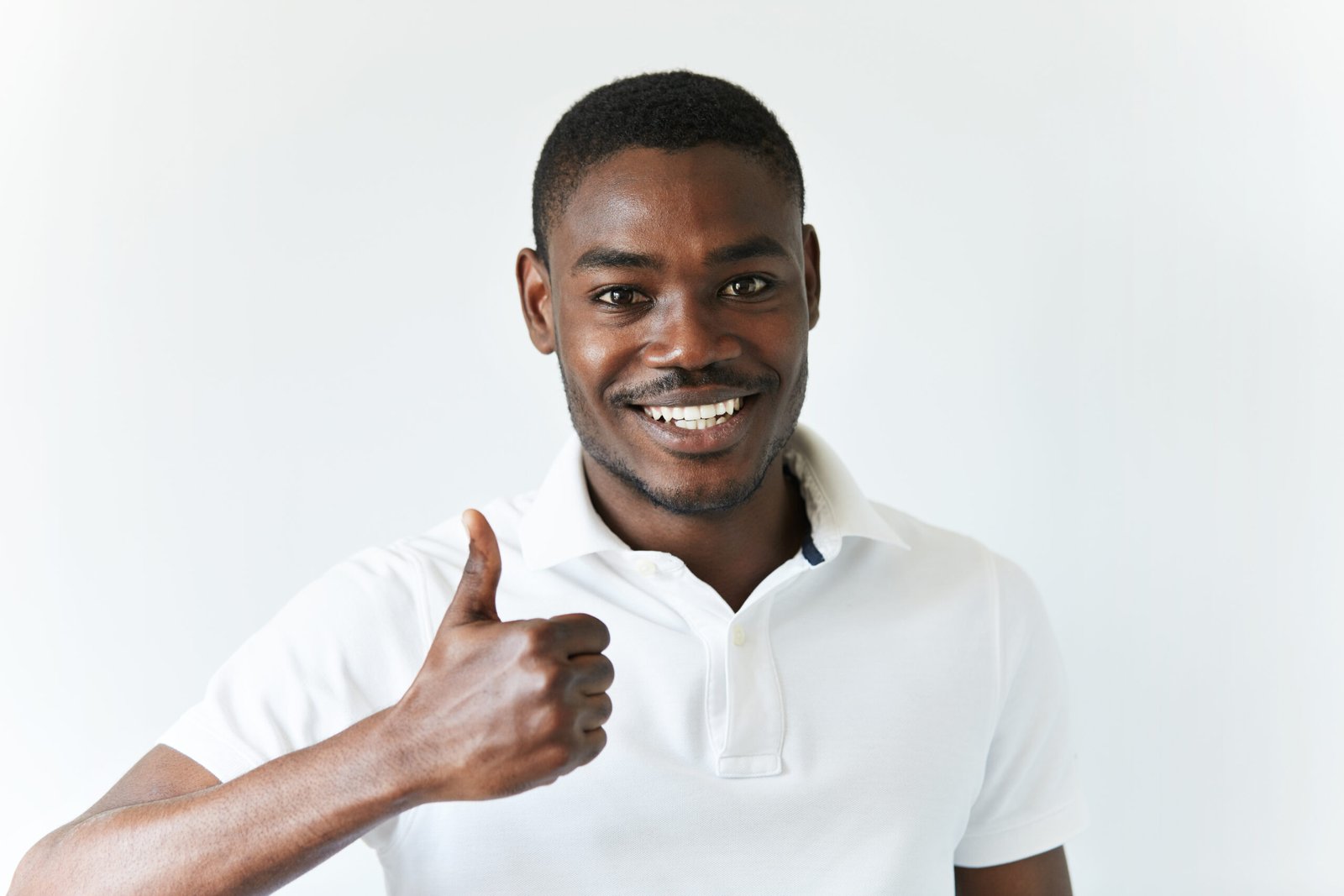 success and achievement. headshot of successful handsome african freelancer gesturing thumbs up, looking with happy cheerful expression, achieving career goals, posing against white studio wall